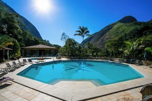 A swimming pool surrounded by lounge chairs and umbrellas, with a mountain backdrop. - Hotel Caminhos de Itaipava (Petrópolis)