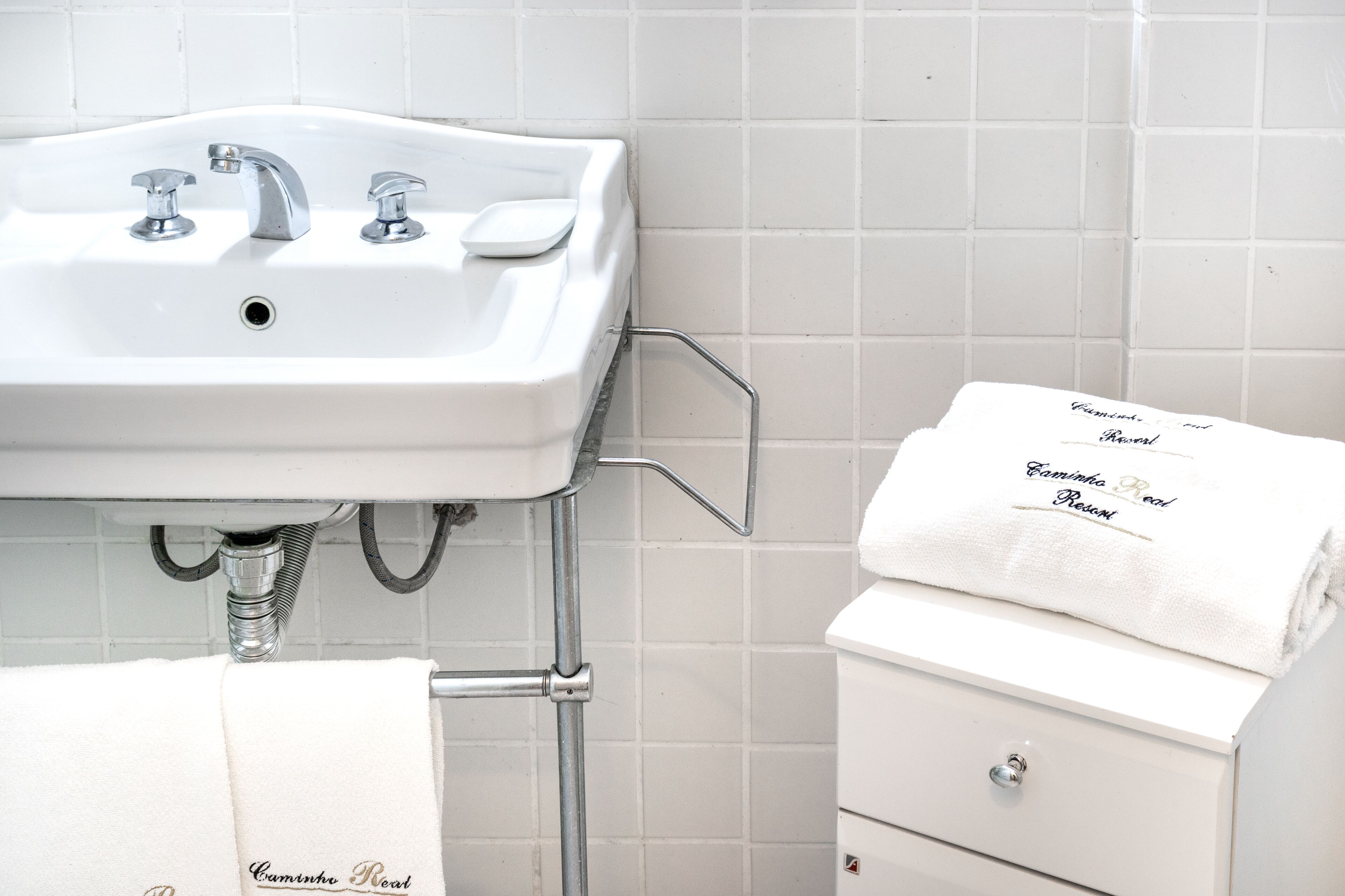 Une salle de bain avec un lavabo blanc, deux robinets et un porte-serviettes sur lequel est posée une serviette pliée.