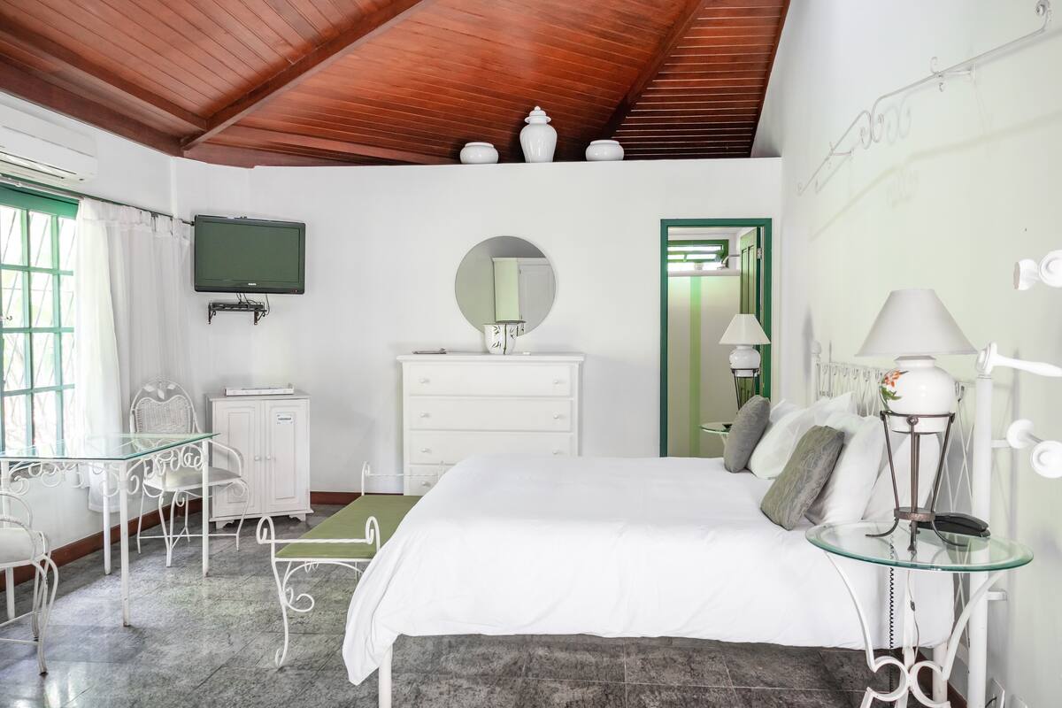 Un dormitorio con cama, cómoda, espejo, televisión y mesa de vidrio.