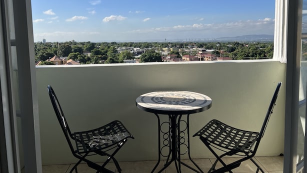 Un balcone con due sedie e un tavolo, affacciato su una zona residenziale con case e vegetazione.
