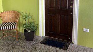 Una porta in legno con stipite bianco, una sedia in vimini con cuscino a righe e una pianta in vaso accanto.