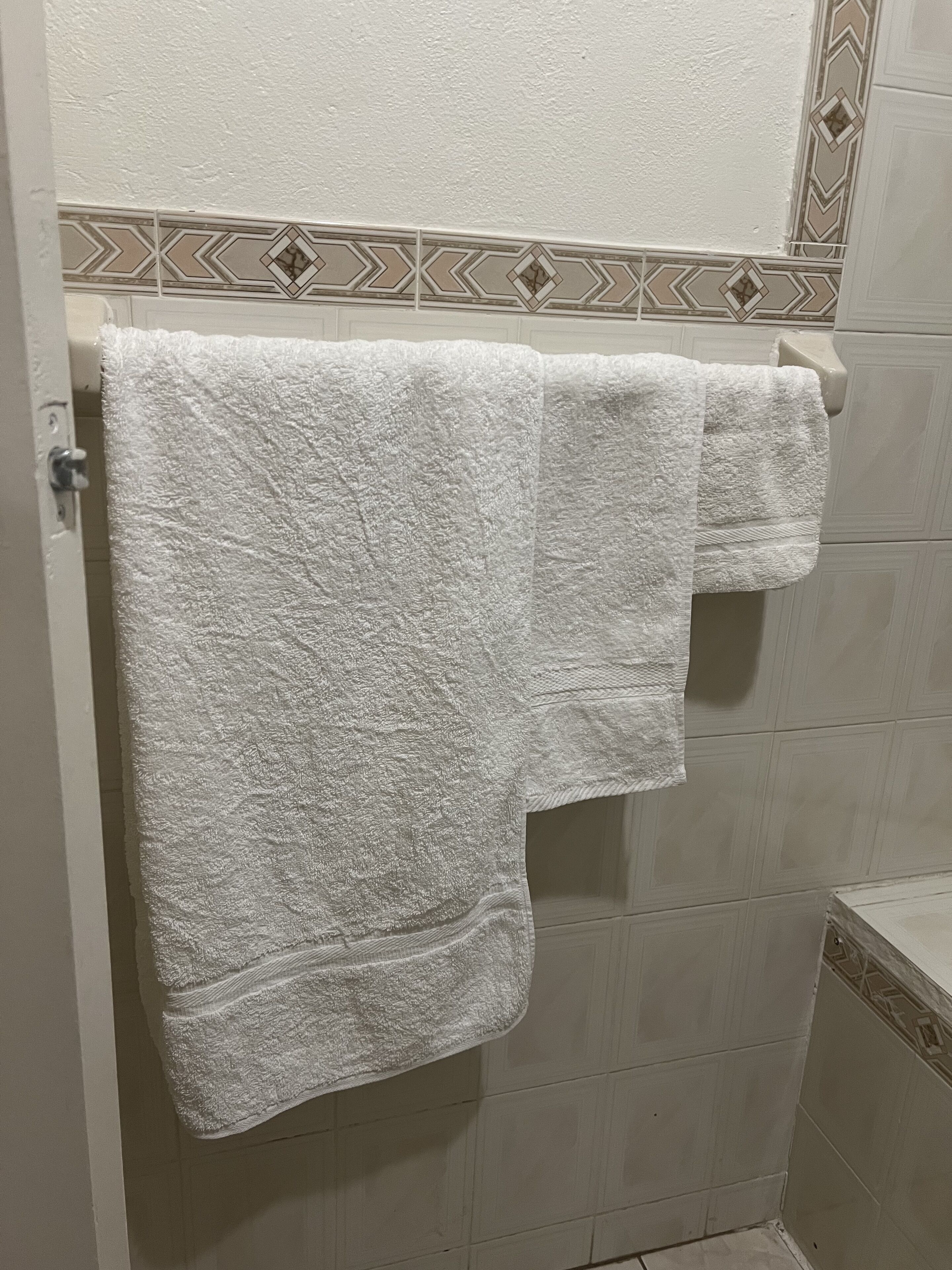 Un baño con una toalla blanca colgada en un perchero, baldosas color beige y una decoración de borde.