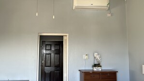 Una stanza con una porta in legno scuro, un condizionatore d'aria bianco fissato al muro, un comò in legno e un'orchidea in vaso.