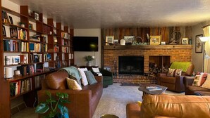 Ein gemütliches Wohnzimmer mit Kamin, Ledersofas, einer Bücherwand und einem Flachbildfernseher.