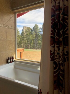 A bathroom with a bathtub, a window, and a view of a forest and a mountain.