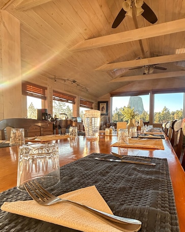 A dining area with a long wooden table set for a meal, large windows offering a view of trees and a mountain, and a ceiling fan.