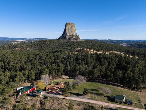 A remote cabin with a red roof, surrounded by dense forest and a prominent rock formation in the background. - Devils Tower Lodge (Bed and Breakfast) (Devils Tower)