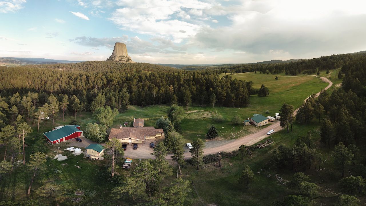 An aerial view of a rural area with a prominent natural landmark in the background, surrounded by dense forests and a few buildings with green roofs.