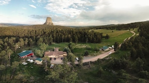 An aerial view of a rural area with a prominent natural landmark in the background, surrounded by dense forests and a few buildings with green roofs.