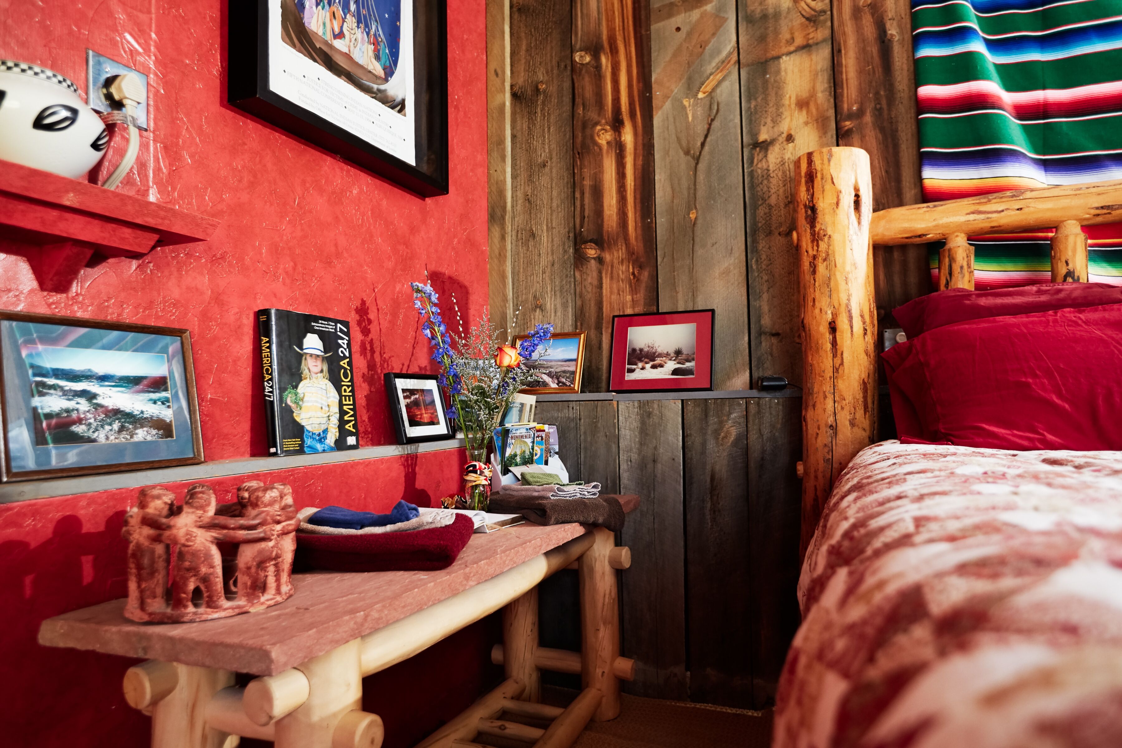 A cozy room with a wooden bed, a red wall, and various framed pictures and decorations.