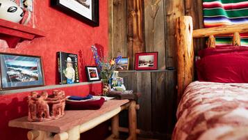 A cozy room with a wooden bed, a red wall, and various framed pictures and decorations.