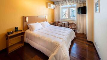 Une chambre d’hôtel avec un grand lit, un bureau avec un téléphone, une chaise, une petite table et un téléviseur fixé au mur.