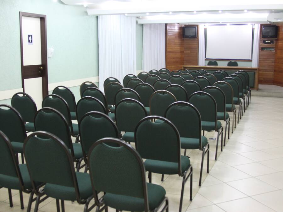 Une salle de conférence avec des rangées de chaises vertes, un tableau blanc et un écran de projection.