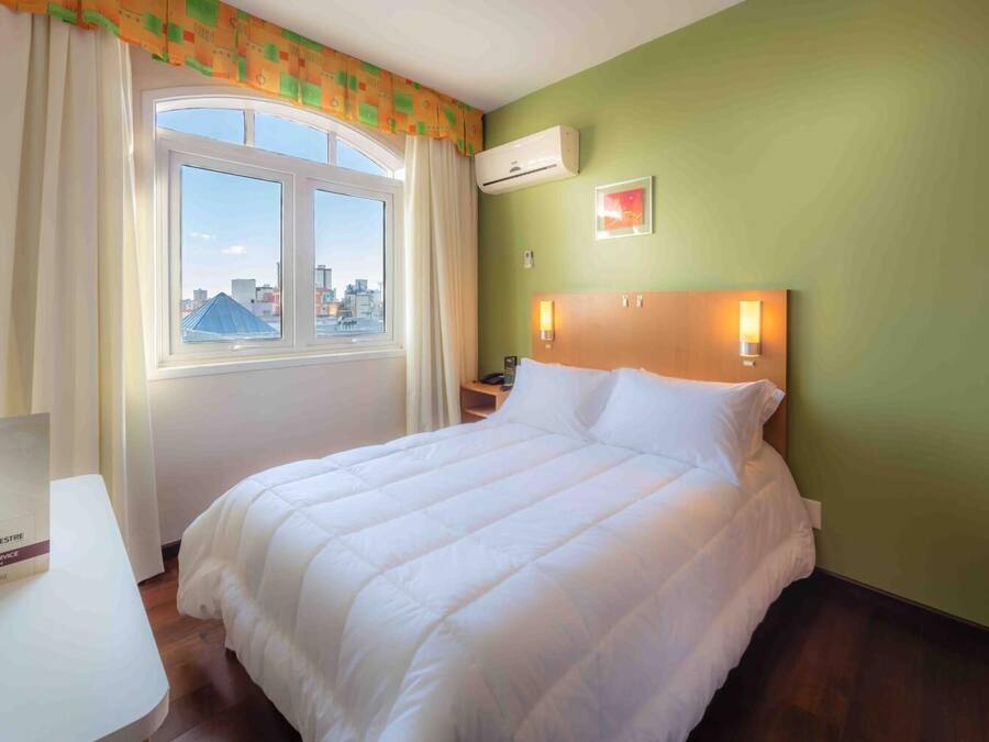 Una habitación de hotel con cama, escritorio y ventana con cortinas.