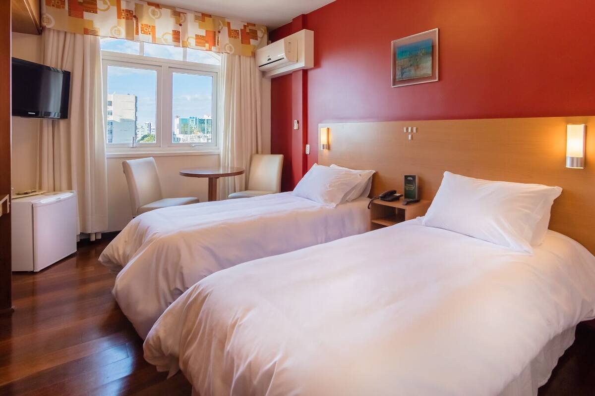 Une chambre d’hôtel avec deux lits, une télévision, un bureau et une fenêtre avec des rideaux.