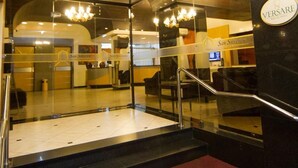 A modern hotel lobby with a glass entrance, a staircase, and a chandelier.