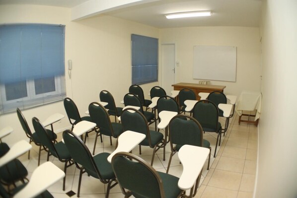 A classroom with rows of green chairs and white desks, a whiteboard, and a wooden table. - San Silvestre Hotel (Passo Fundo)