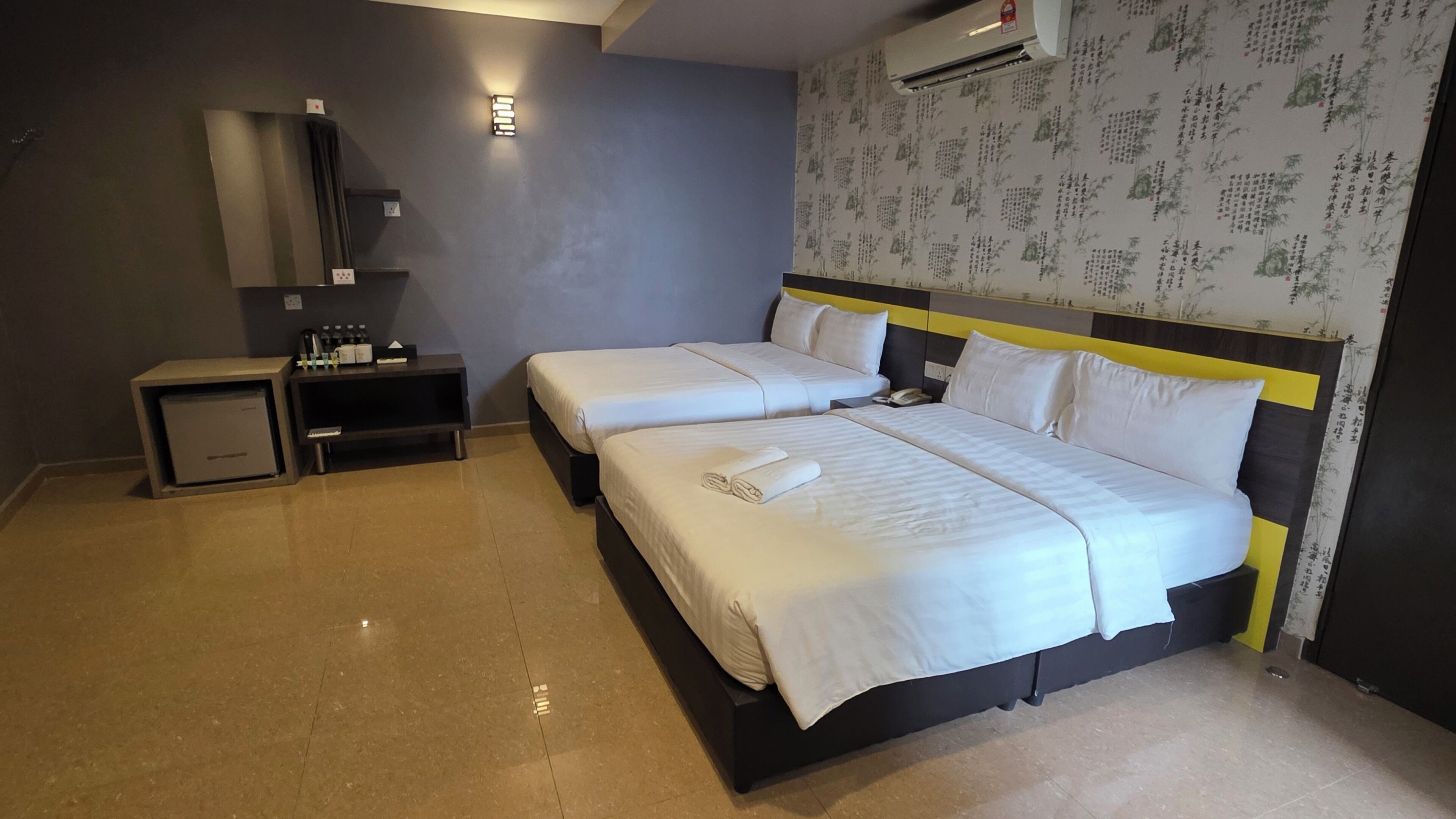 Une chambre d’hôtel avec deux lits, une table de chevet, un petit bureau et un climatiseur fixé au mur.