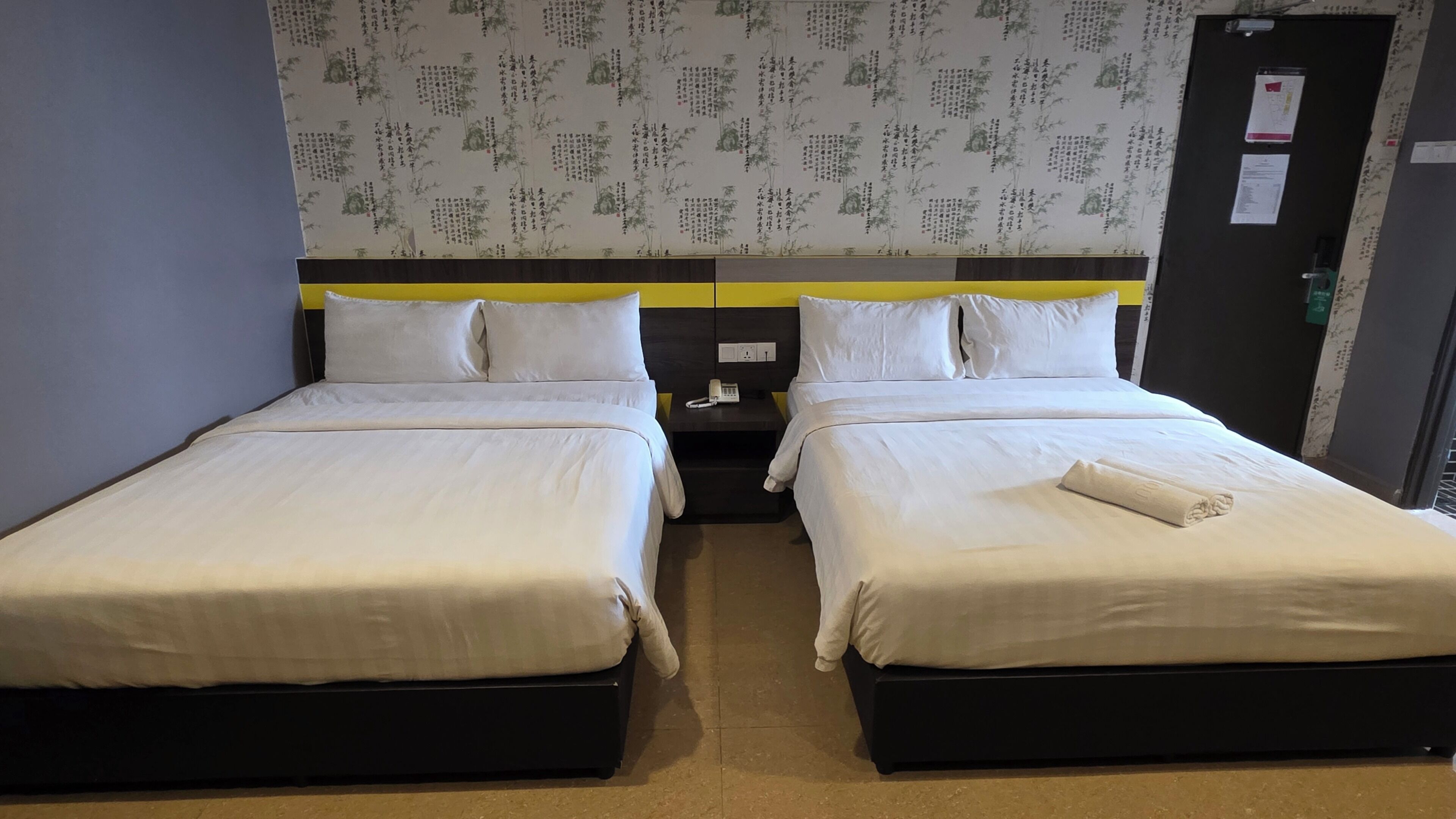 A hotel room with two beds, a nightstand with a phone, and a wall with a patterned design.