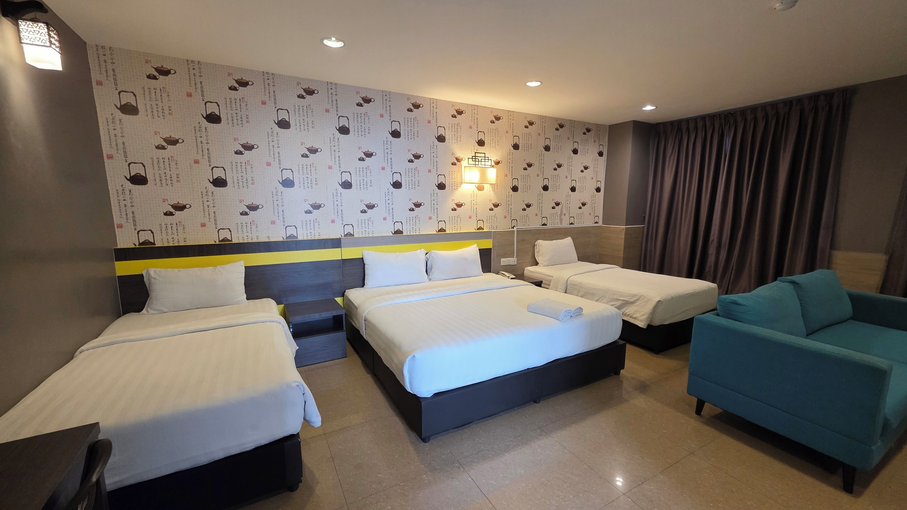 A hotel room with three beds, a sofa, and a wall with a pattern of teapots.