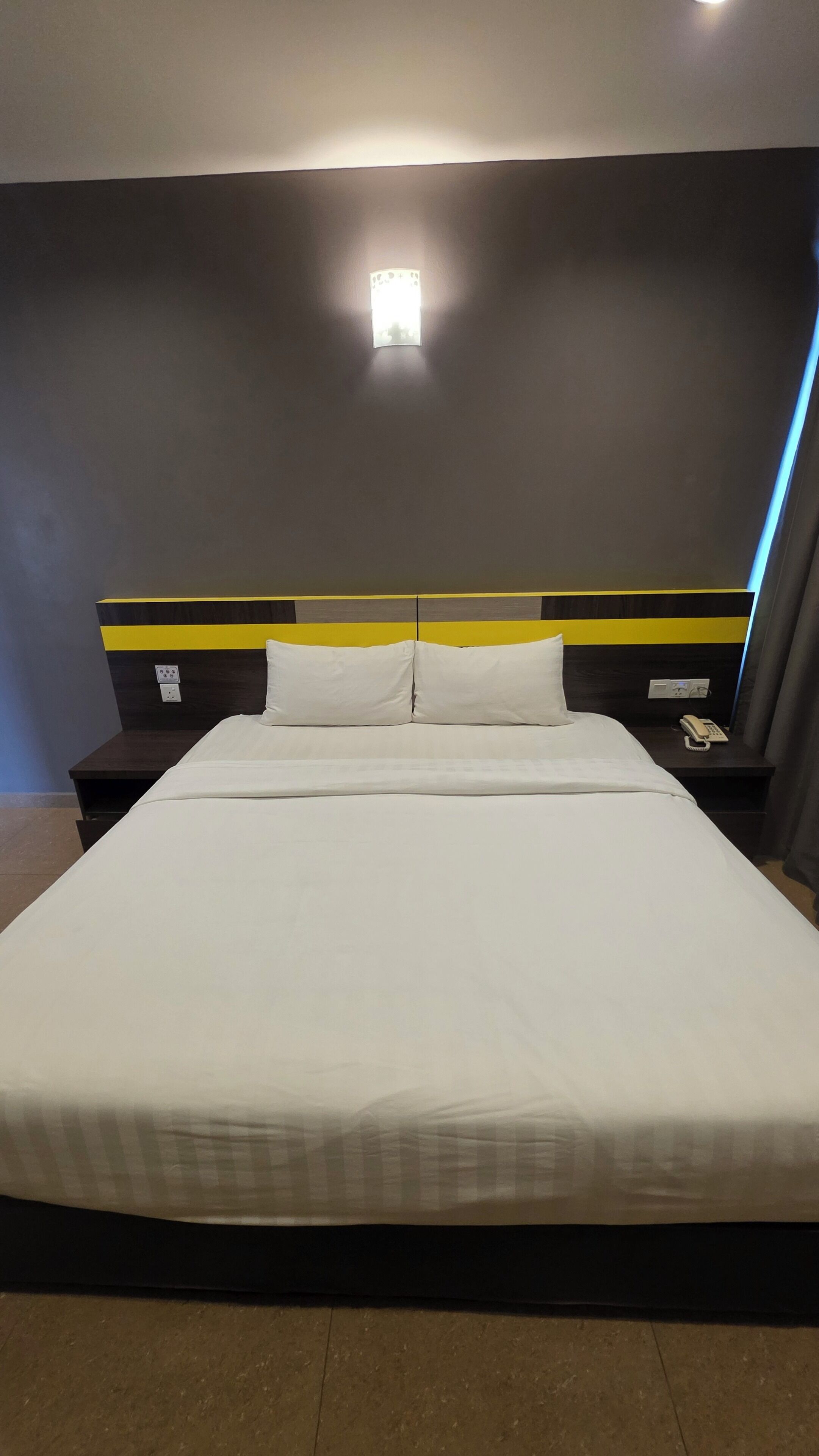 Habitación de hotel con una cama grande, una mesita de noche con teléfono y una lámpara en la pared.