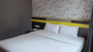Habitación de hotel con cama, aire acondicionado de pared, mesita de noche con teléfono y pared decorada con motivos de monumentos famosos.