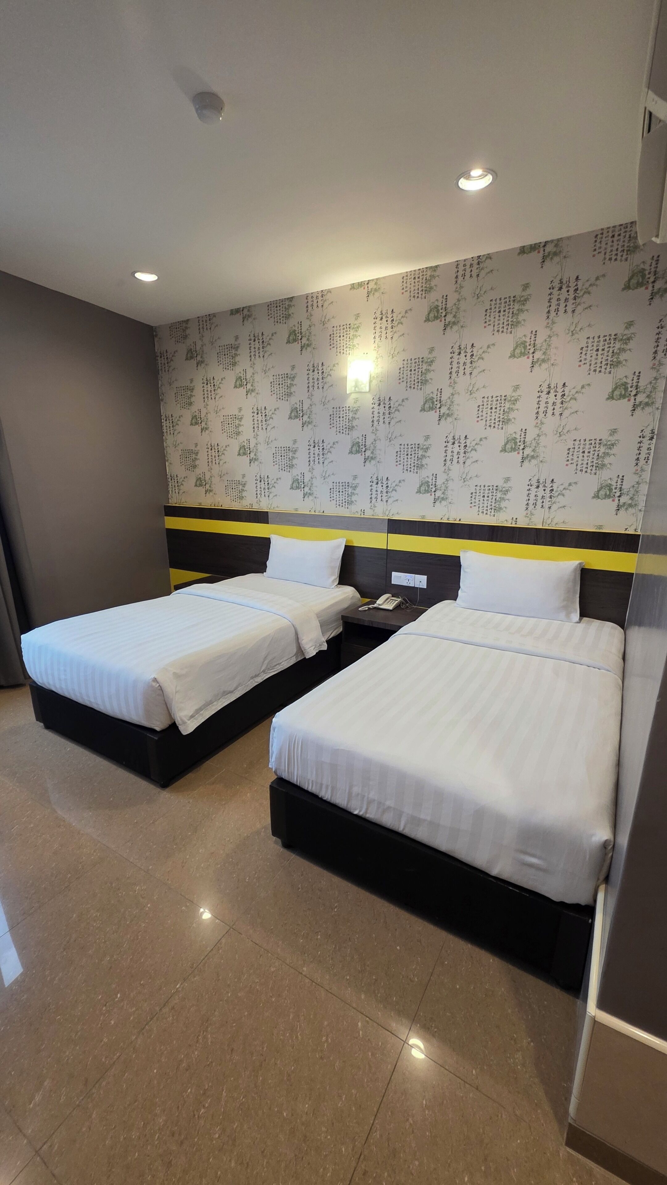 A hotel room with two beds, a nightstand, and a wall with decorative patterns.