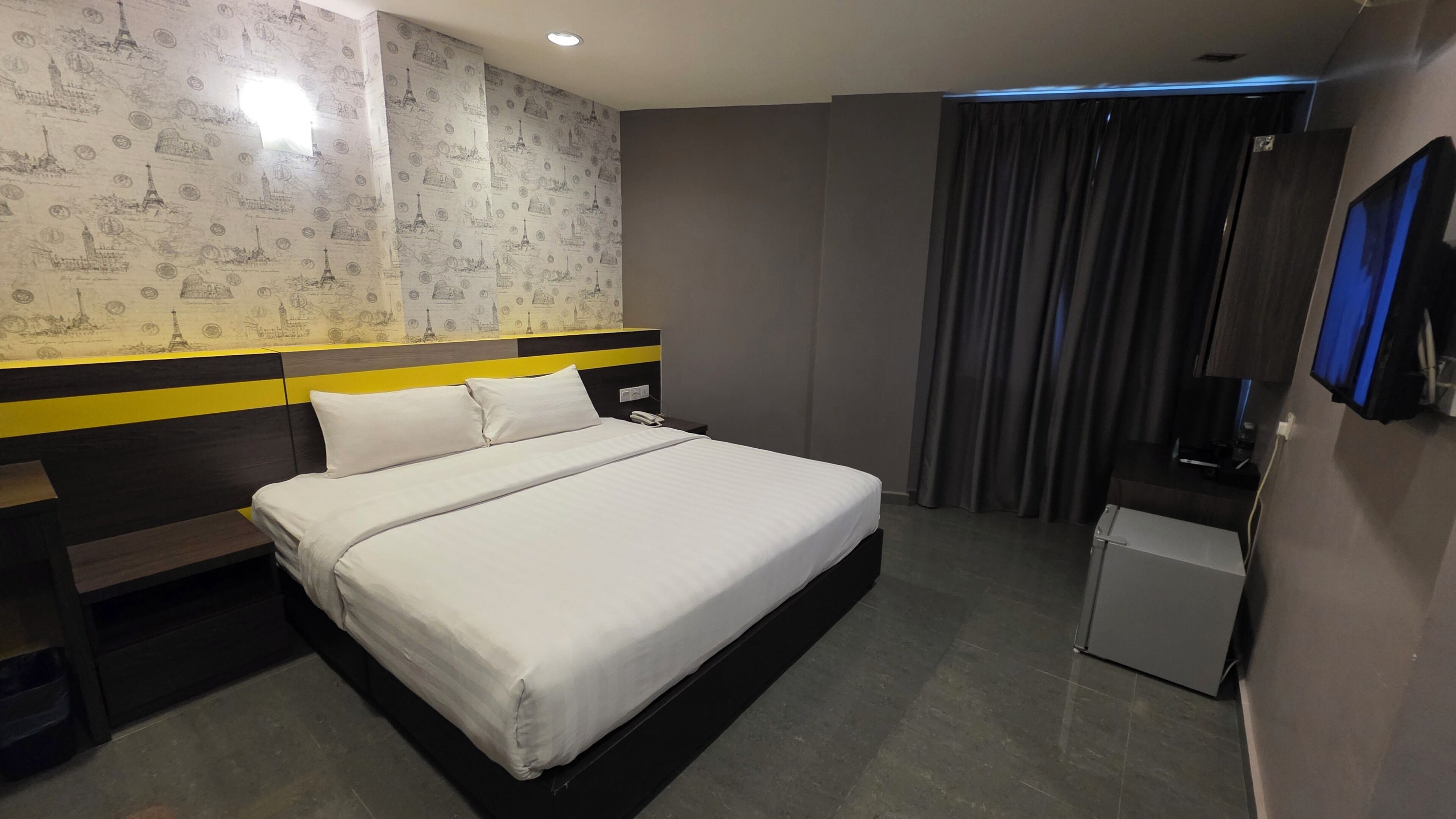 Une chambre d’hôtel avec un lit, un bureau, un petit réfrigérateur et un rideau.