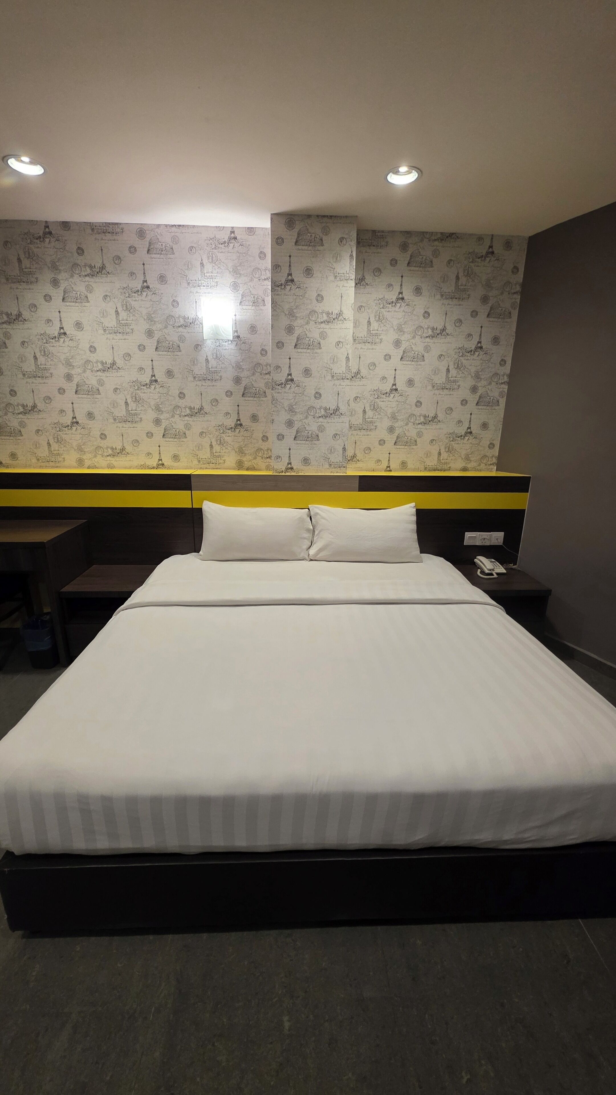 Une chambre d’hôtel avec un lit, une table de chevet, une commode et un mur recouvert d’un papier peint à motifs.