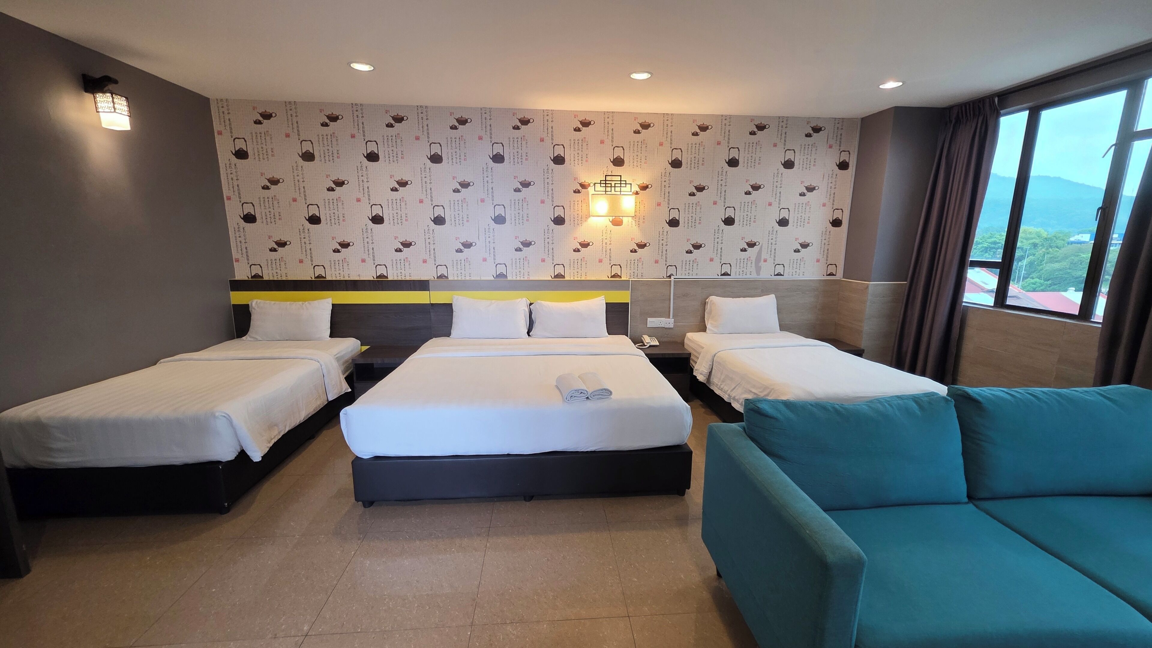 Habitación de hotel con dos camas, un sofá, un papel tapiz estampado y vistas a través de la ventana.