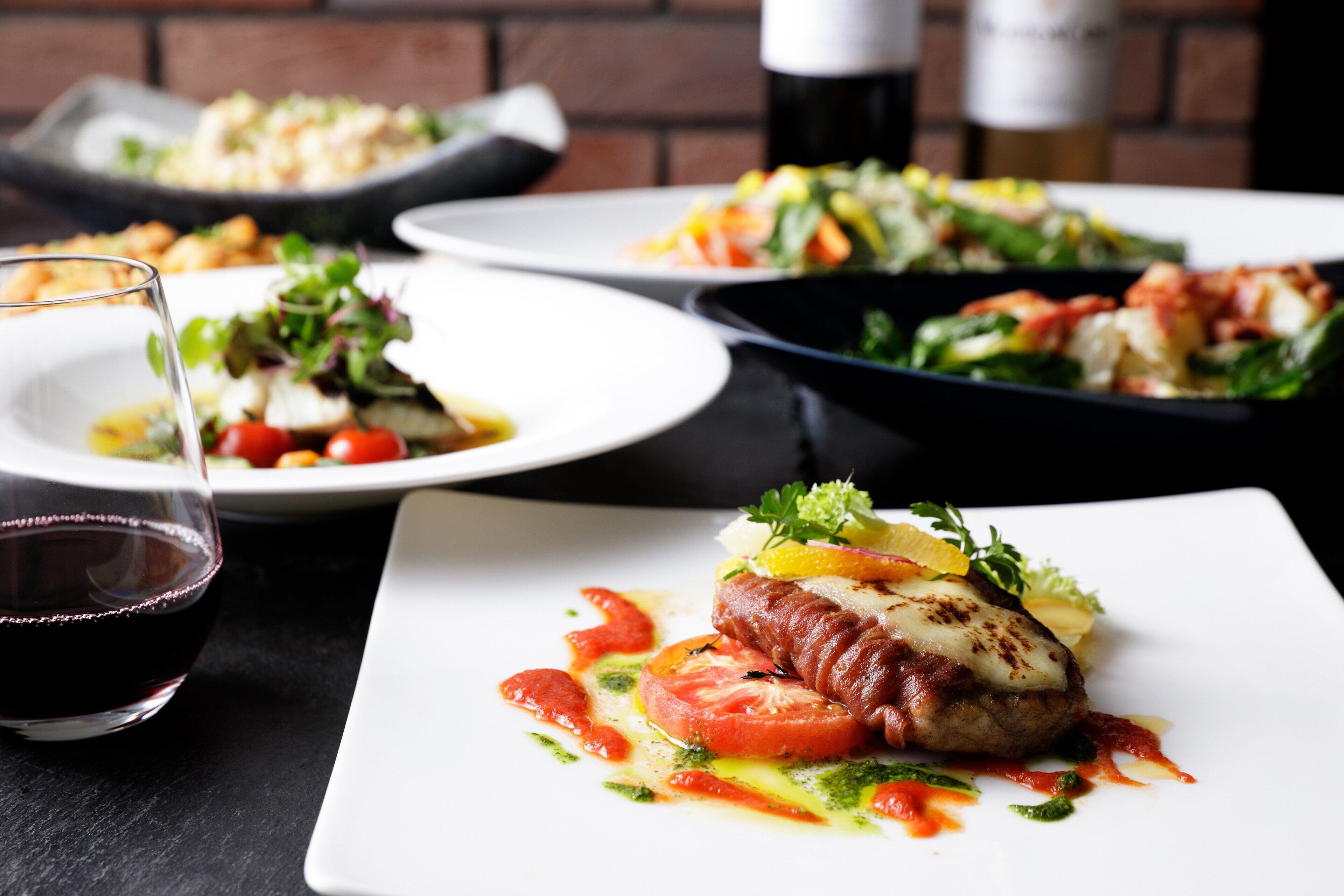 A dining table with plates of food, a glass of red wine, and a black skillet in the background.