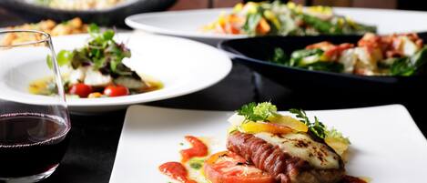 A dining table with plates of food, a glass of red wine, and a black skillet in the background.