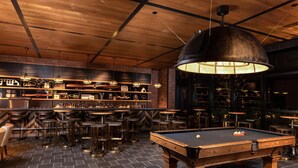 Een biljarttafel in een bar, met krukken en flessenrekken.