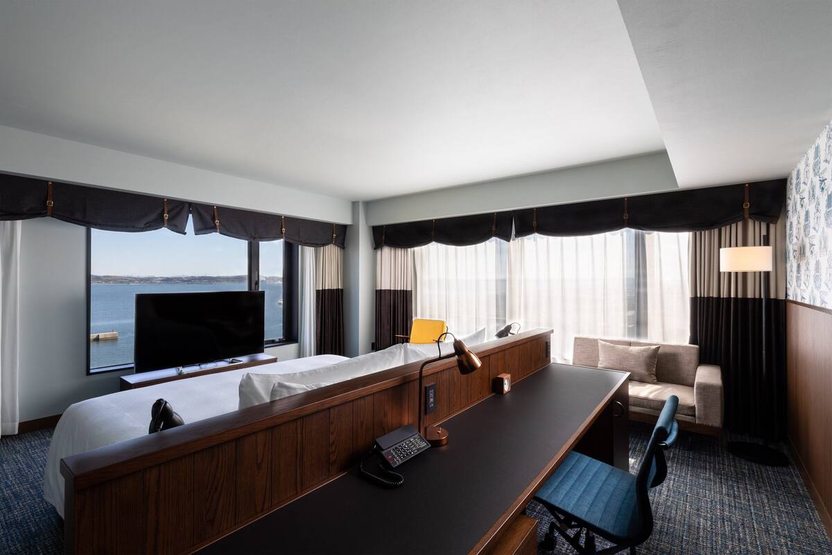 Une chambre d’hôtel avec un grand lit, un bureau avec un téléphone, une chaise, une télévision et une vue sur la mer.