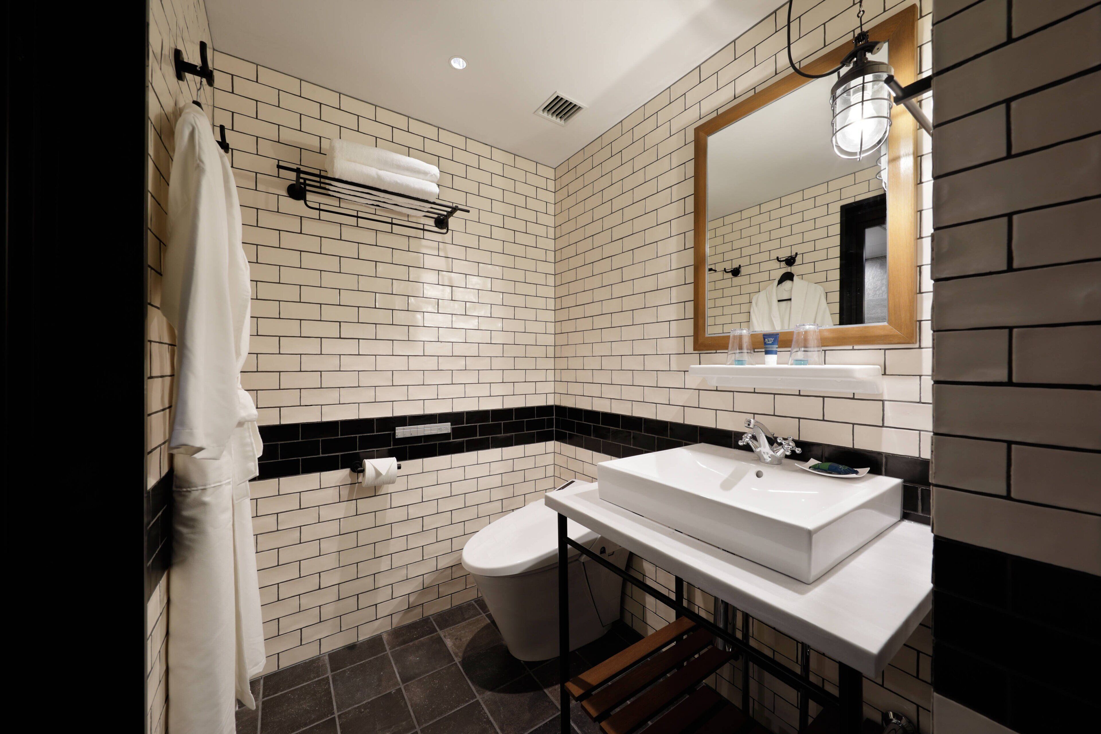 Un baño moderno con paredes de baldosas blancas y negras, un lavamanos blanco y un espejo.