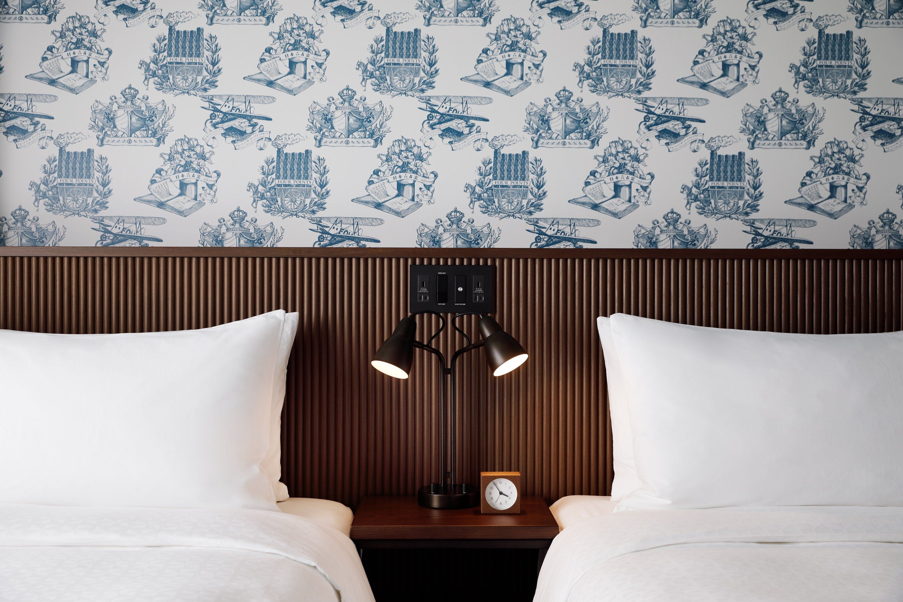 Una habitación de hotel con dos camas, una mesita de noche con lámpara y un reloj.