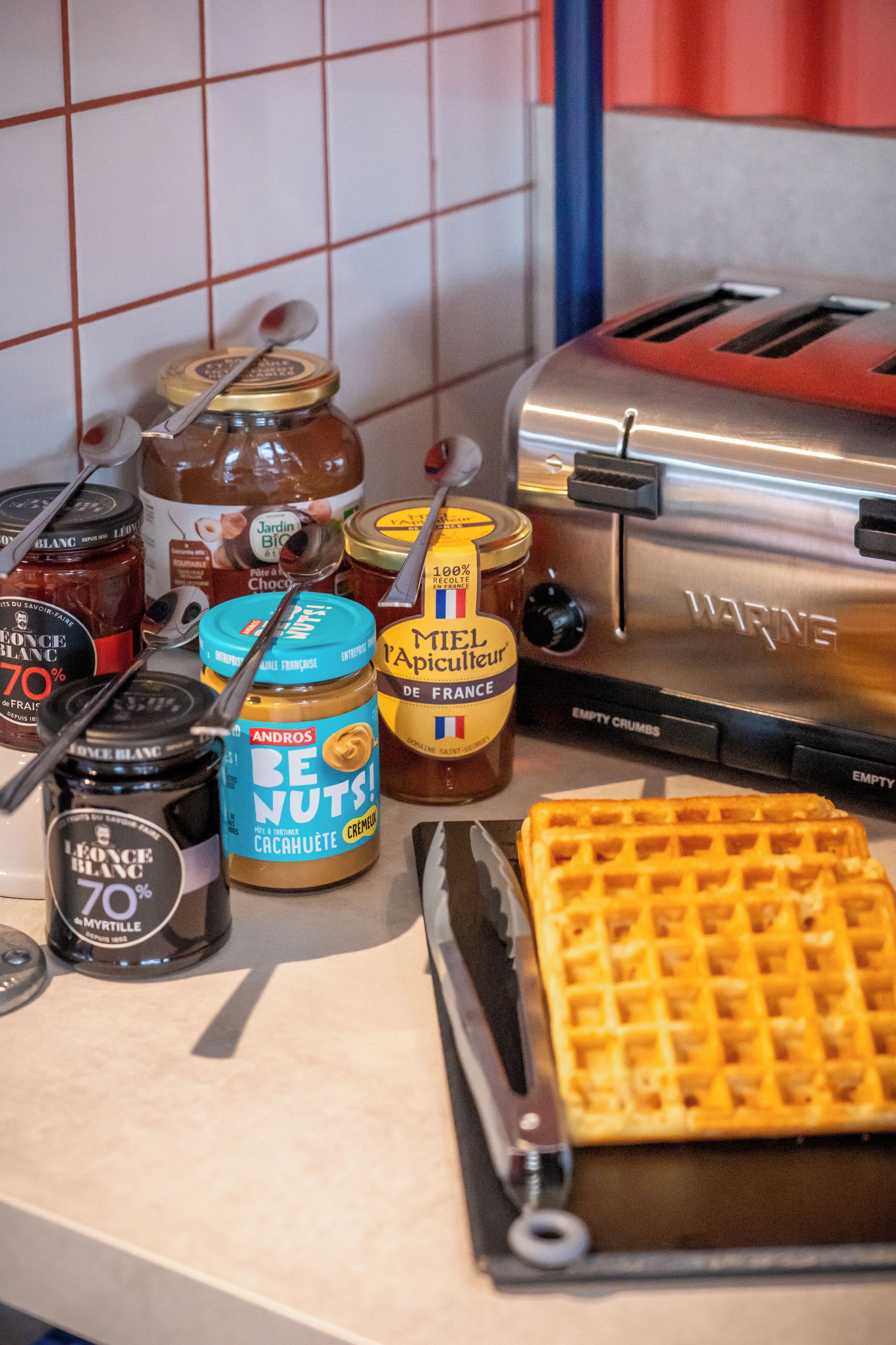 Eine Küchenarbeitsplatte mit verschiedenen Lebensmitteln, darunter Honiggläser, Senf und andere Würzmittel, ein Waffel und ein Toaster.