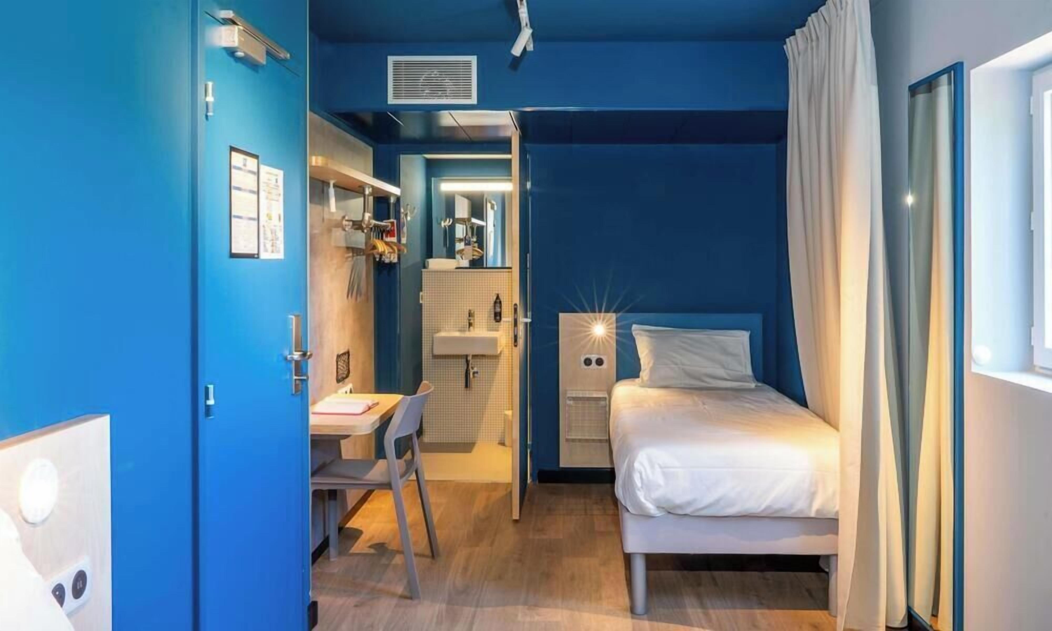 Habitación de hotel con cama, escritorio y baño visible a través de una puerta abierta.