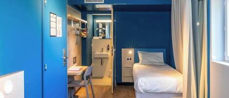 Habitación de hotel con cama, escritorio y baño visible a través de una puerta abierta.