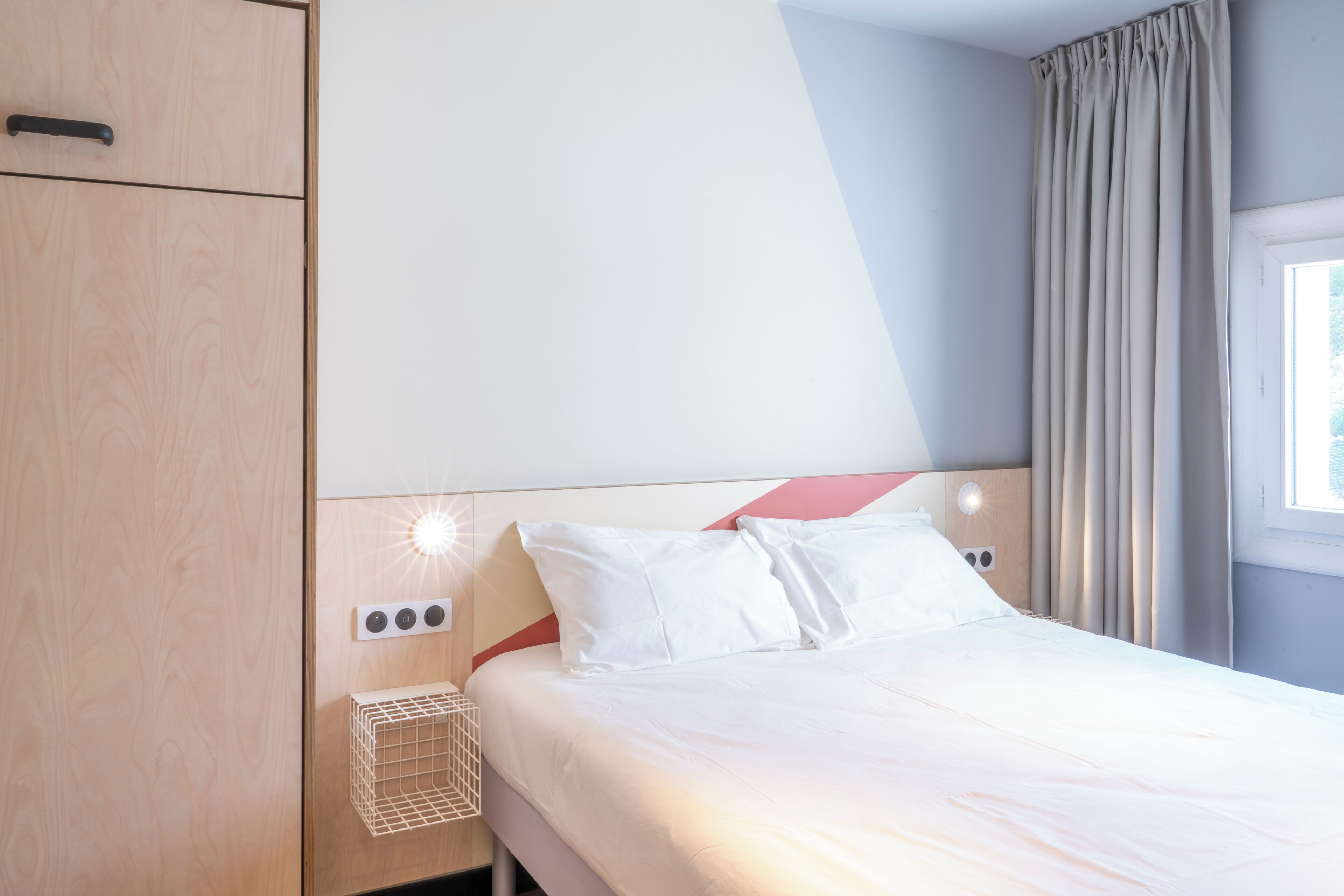 Une chambre d’hôtel avec un lit, une armoire, une table de chevet avec une lampe et une fenêtre avec des rideaux.