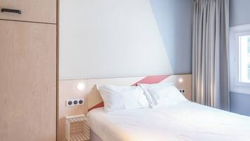 Une chambre d’hôtel avec un lit, une armoire, une table de chevet avec une lampe et une fenêtre avec des rideaux.