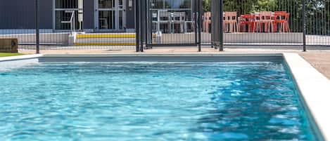 Une piscine entourée d’une clôture, un bâtiment avec une enseigne et des sièges à l’extérieur.