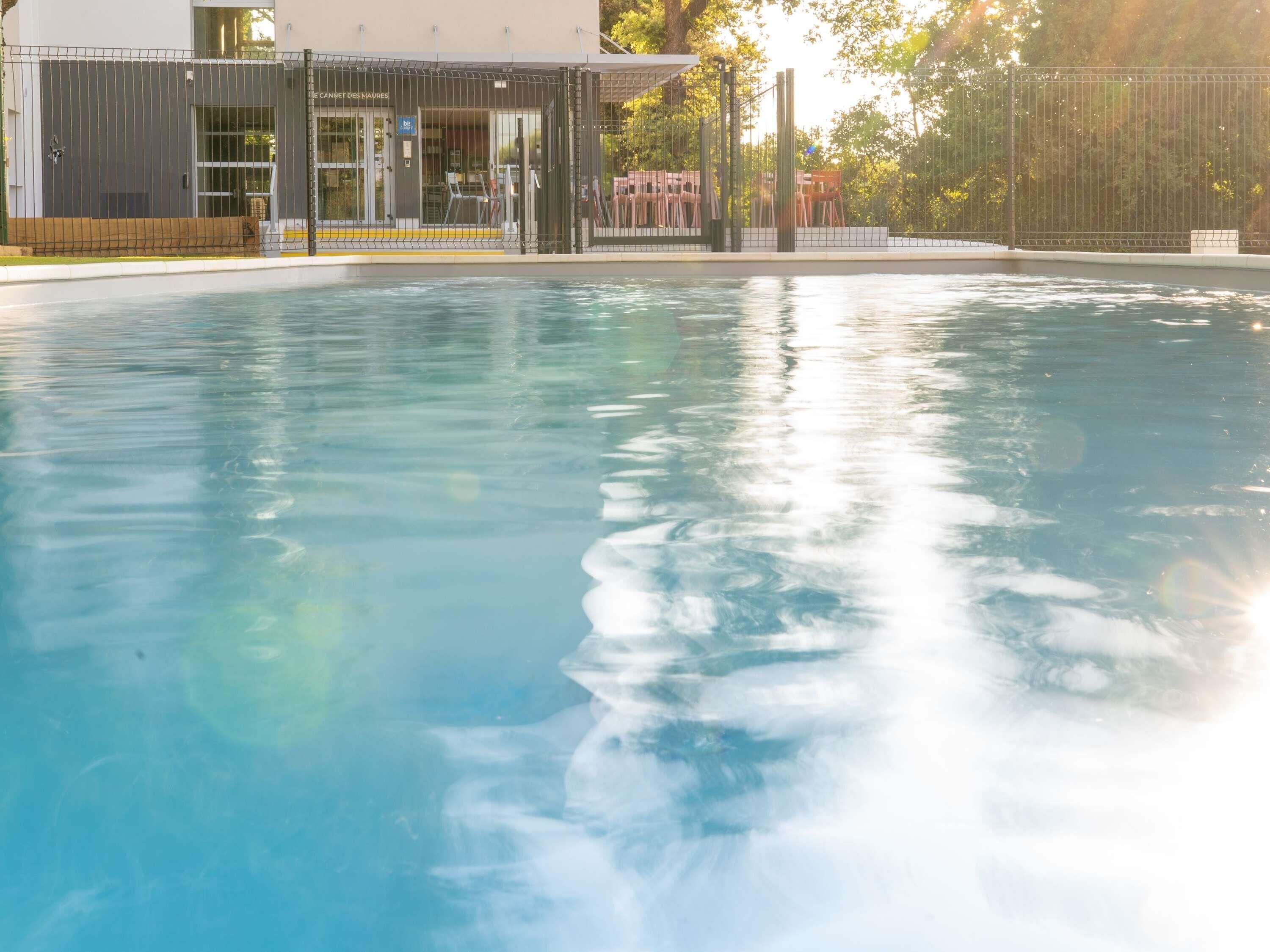 Une piscine entourée d’une clôture, un espace couvert avec des chaises et un bâtiment portant une enseigne.