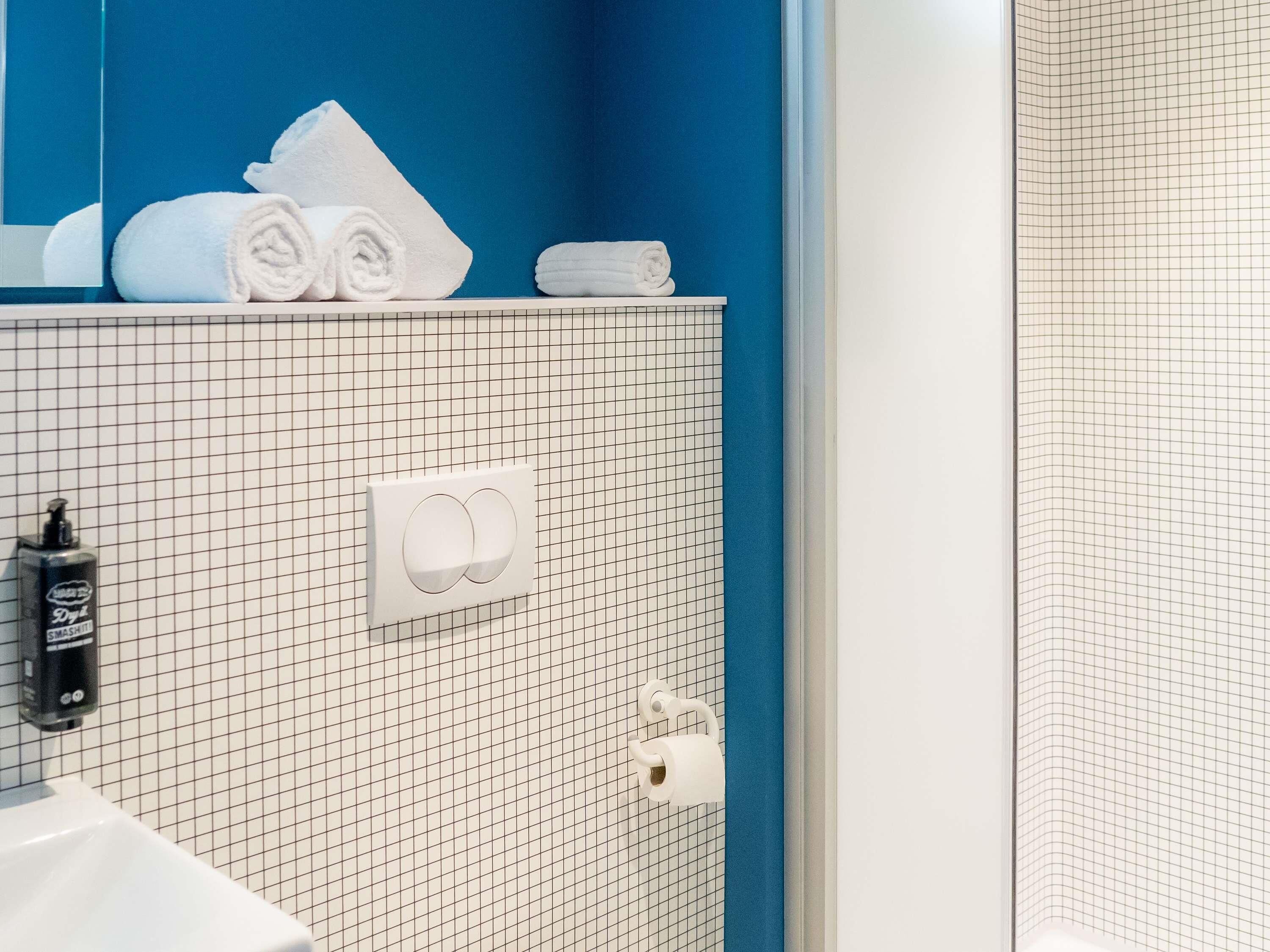 Un baño con pared azul, suelo de baldosas formando un diseño de cuadrícula, lavamanos blanco, dispensador de toallas y porta papel higiénico.