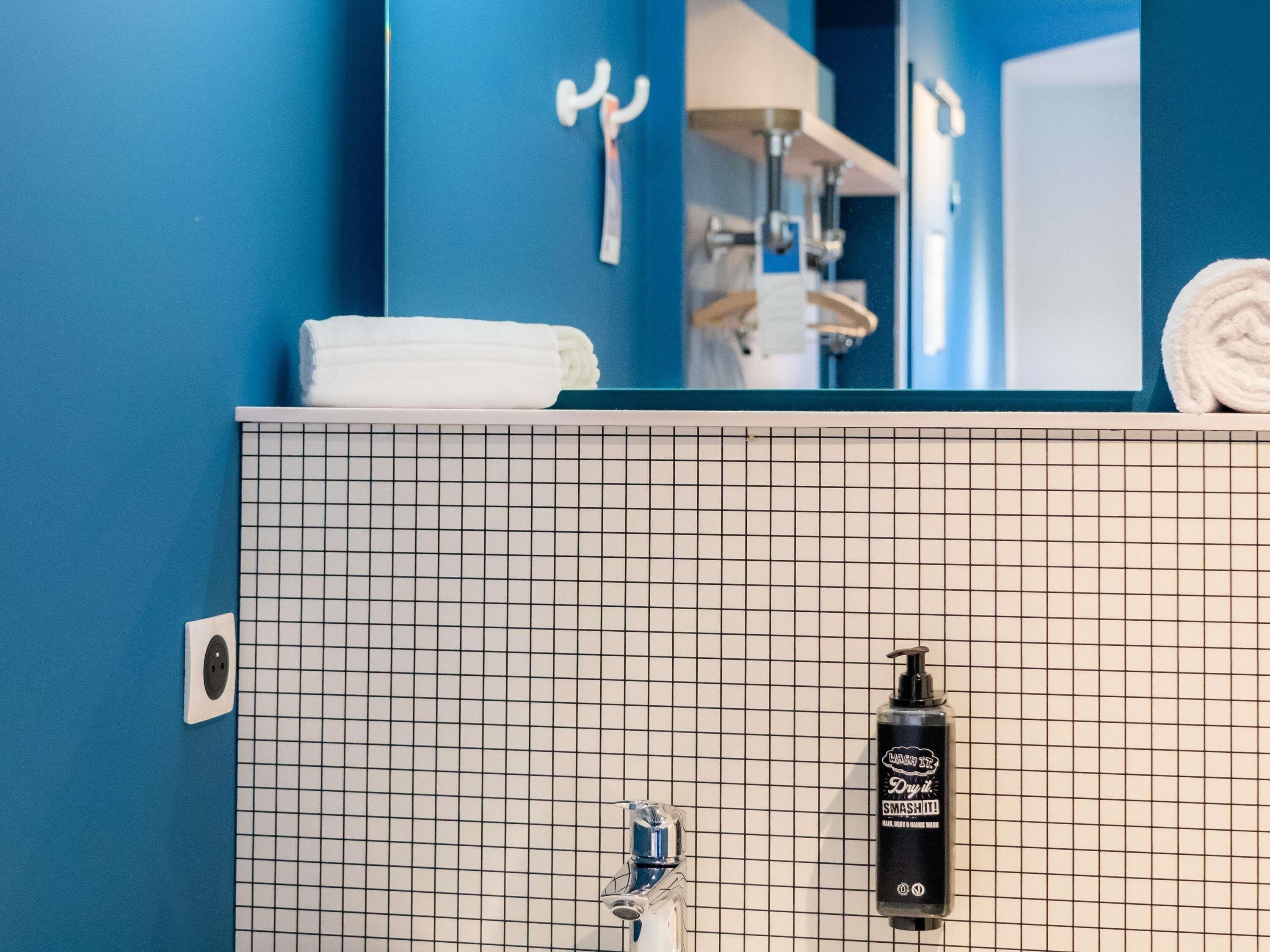 Et badeværelse med blå vægge, en hvid flisesink, et håndklæde og en shampoo-flaske.