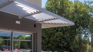 An outdoor patio with tables and chairs, a covered seating area, and a view of trees and a parking lot. - ibis budget Le Cannet des Maures (Le Cannet-des-Maures)