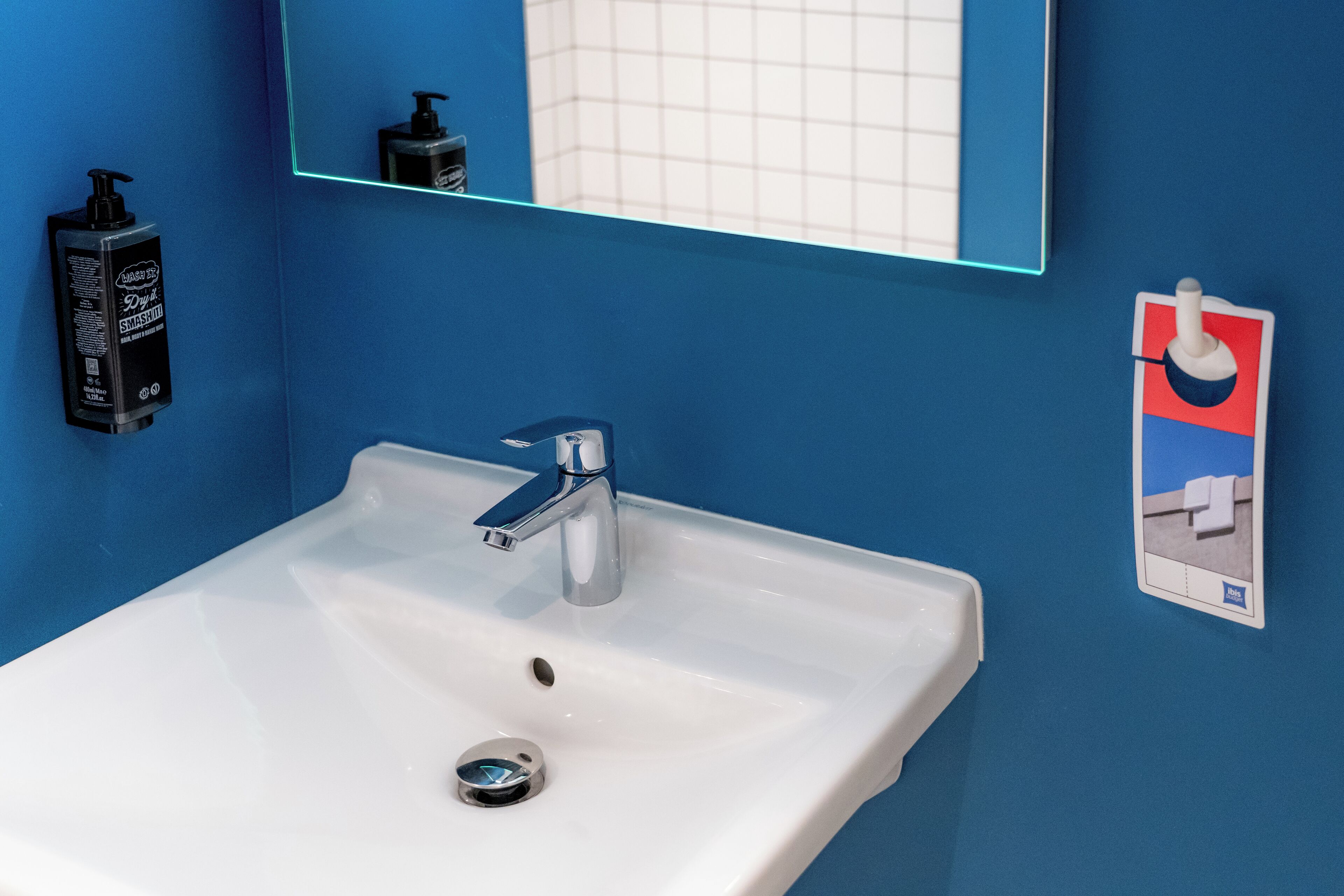 Un baño con lavamanos blanco, paredes azules, un espejo y dispensador de jabón.