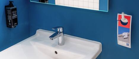 Un baño con lavamanos blanco, paredes azules, un espejo y dispensador de jabón.