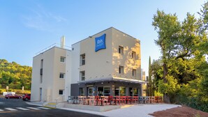 A modern building with a sign reading "ibis budget." It features a covered outdoor seating area with tables and chairs. - ibis budget Le Cannet des Maures (Le Cannet-des-Maures)