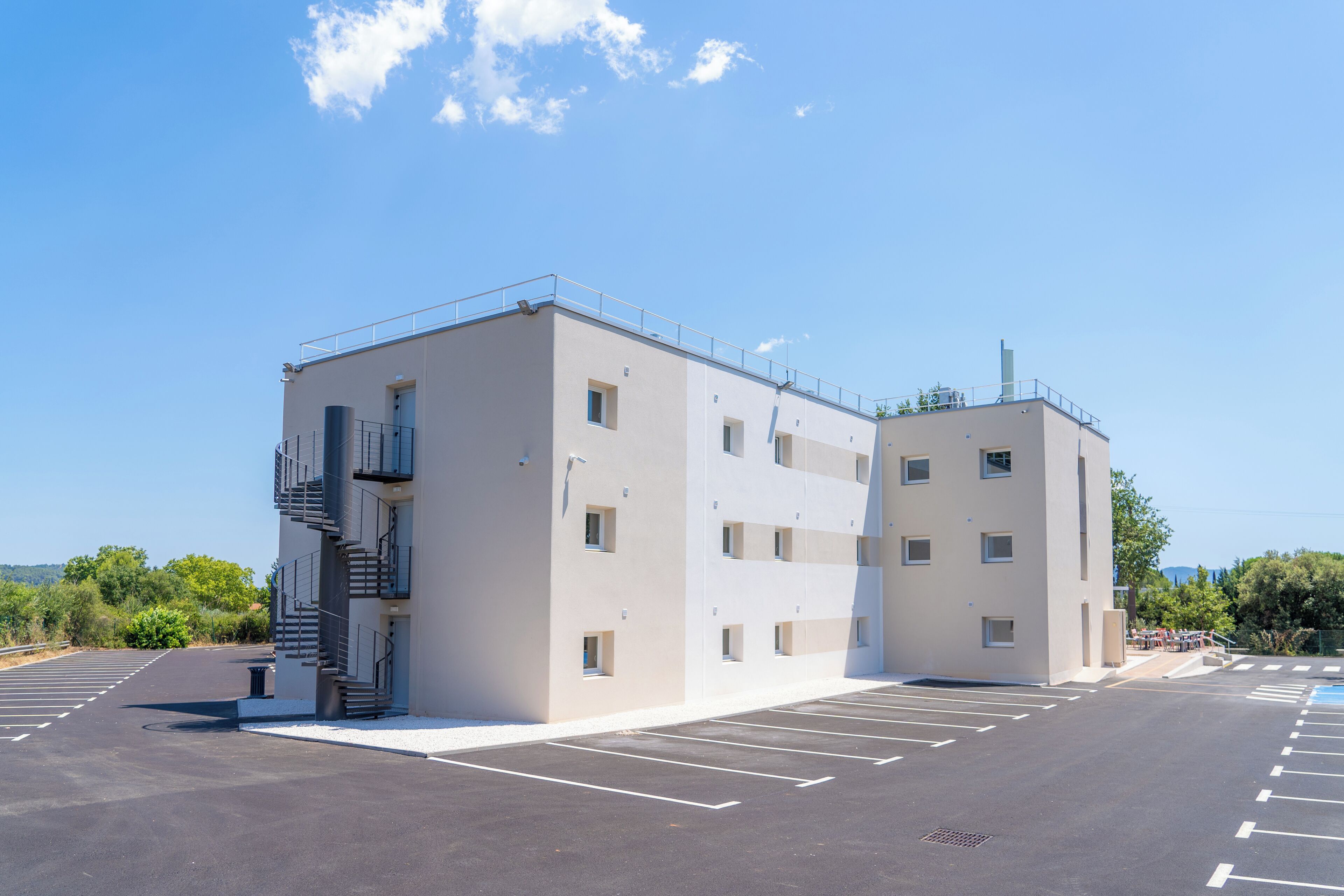 A modern building with a parking lot, a staircase, and a clear sky.